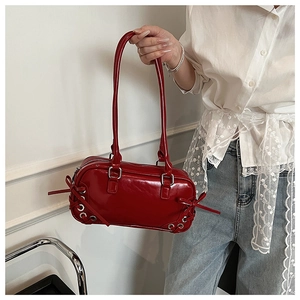 Detail view of glossy red shoulder bag with decorative side bows and metallic eyelets