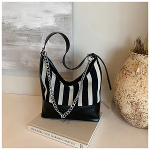 Detail of striped canvas shoulder bag with silver chain on artistic background