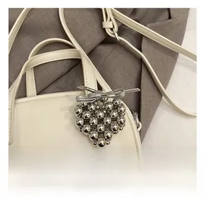 Détail d'un charm de sac en forme de cœur argenté avec nœud sur sac en cuir blanc cassé