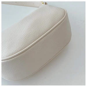 Detail of lychee pattern leather texture and gold hardware on cream shoulder bag