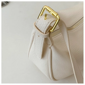 Detailed macro view of cream leather texture and gold metal buckle on the saddle bag strap