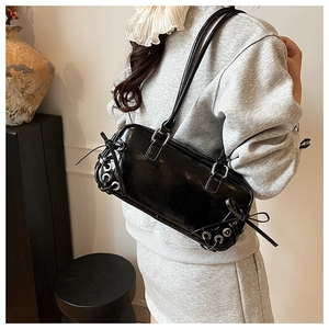Dettaglio della borsa a spalla in pelle verniciata nera con occhielli e fiocchi decorativi