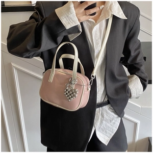 Détail du sac bandoulière en cuir verni rose et blanc avec pendentif cœur argenté
