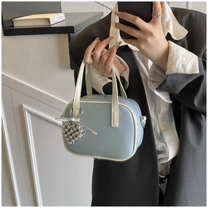 Détail du sac à main en cuir verni bleu clair avec anses crème et breloque en cœur