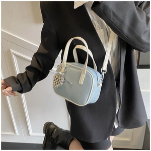 Détail du sac à main bleu clair en cuir verni avec breloque argentée et poignée blanche