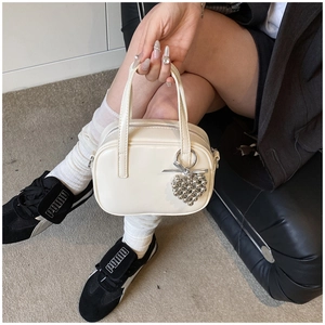 Détail d'un mini sac bowling beige avec breloque cœur et finitions métalliques argentées