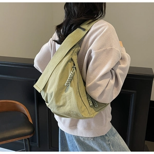 Detail of light green nylon crescent crossbody bag with woven zipper pull on model