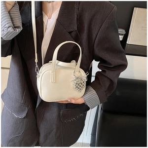 Détail d'un sac bandoulière blanc crème en cuir avec breloque cœur sur le mannequin