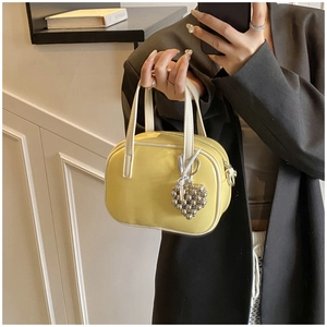 Détail d'un mini sac à main jaune vif avec poignées blanches et breloque coeur en perles
