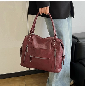 Detail of burgundy vintage tote bag with multiple silver zippers and rivets on soft leather