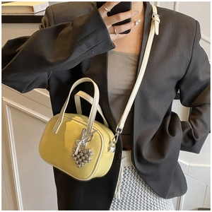 Détail du petit sac jaune avec bordure blanche et breloque cœur porté par un mannequin