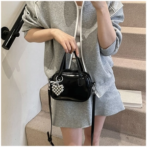 Détail du sac à main noir brillant avec breloque cœur argentée et bandoulière réglable
