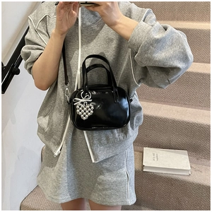 Détail du sac en cuir verni noir brillant avec breloque cœur argentée et nœud décoratif