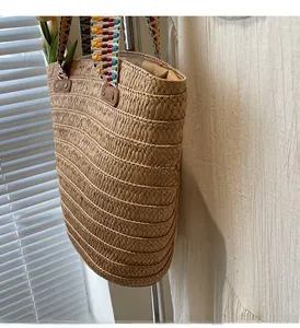 Detail of hand-woven straw tote bag featuring a colorful geometric jacquard shoulder strap