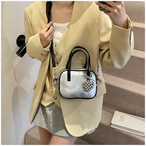 Détail du sac argenté métallisé avec poignées noires et pendentif cœur sur le mannequin