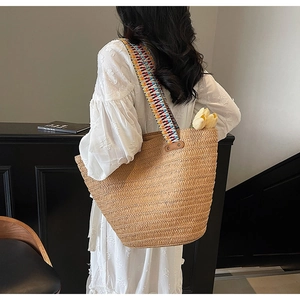 Detail of woven straw tote bag featuring a colorful wide patterned strap and large capacity