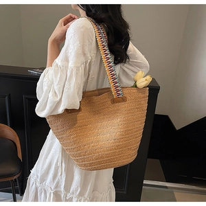 Detail of handwoven straw tote bag featuring a colorful ethnic style wide shoulder strap