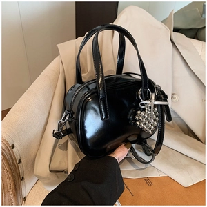 Détail du sac à main noir brillant avec breloque cœur sur fond en tissu beige