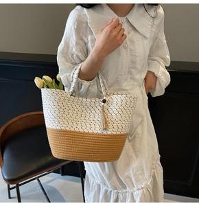 Close-up of dual-tone woven tote bag with tassel detail and delicate floral props