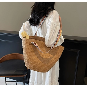 Detail view of woven straw tote bag featuring colorful geometric embroidery shoulder strap