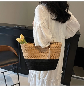Close-up of woven straw tote bag with black contrast base and long tassel charms