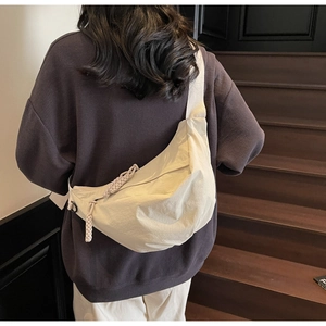 Detail of a cream nylon crescent bag with a decorative braided zipper pull and wide strap