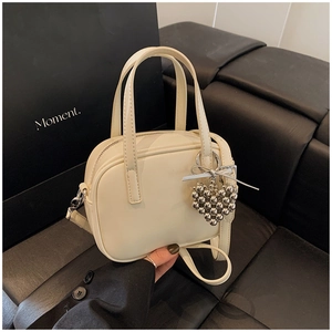 Détail du sac en cuir blanc cassé avec pendentif coeur argenté sur fond en cuir noir