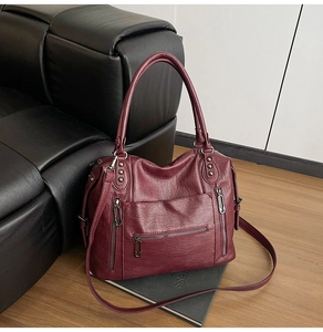 Detail view of burgundy leather tote bag with silver zippers and rivets on sofa