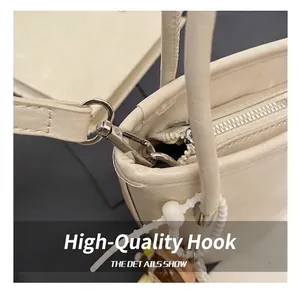 Dettaglio del gancio argentato e zip su borsa in pelle PU color crema con perline bianche