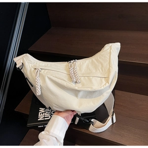 Detail of cream nylon crescent crossbody bag with braided zipper pull on wooden stairs