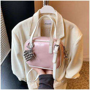 Détail d'un sac à main rose et blanc avec un pendentif fraise argenté sur un costume