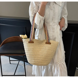 Close-up of woven straw beach bag featuring colorful shoulder straps and rivet details