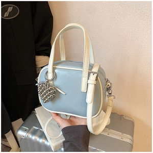 Détail du sac bandoulière bleu clair avec breloque argentée et poignées crème contrastées