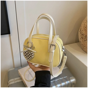 Détail du sac à main jaune en cuir verni avec breloque cœur argentée et nœud