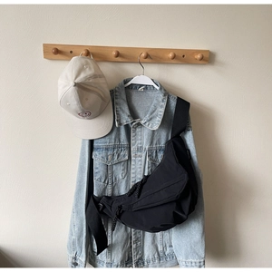Detail of black nylon crescent bag over denim jacket with adjustable strap and woven zipper