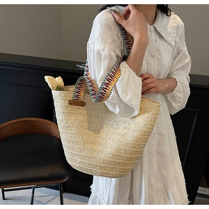 Detail of hand-woven straw tote with colorful geometric handle shown on shoulder