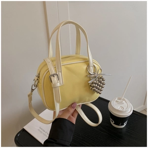 Détail d'un sac à main en cuir jaune clair avec breloque raisin et bandoulière amovible