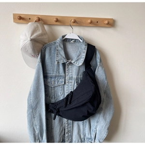 Detail of a black nylon crescent sling bag hung over a blue denim jacket on a hook