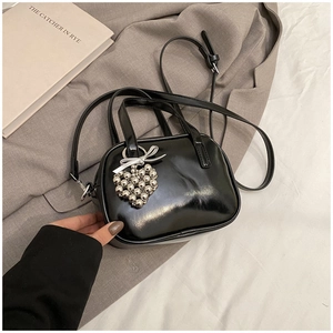 Détail d'un sac à bandoulière noir brillant avec breloque cœur argentée et un nœud
