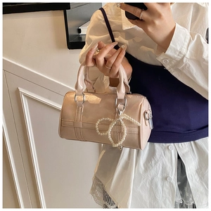 Detailed view of glossy cream cylinder handbag with a pearl bow charm and metal zippers