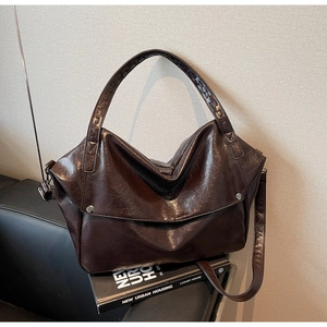 Detail view of large dark brown retro tote bag in glossy leather on a black chair