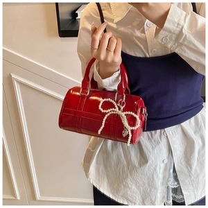 Detail of red patent leather pillow bag featuring pearl bow and silver heart pendant