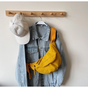 Detail of a yellow nylon crescent bag with braided zipper pulls over a denim jacket