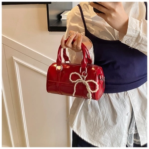 Close-up of red patent leather pillow handbag with pearl woven bow charm and silver hardware