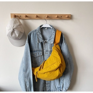 Detail of yellow nylon crossbody bag with woven zipper on a denim jacket background