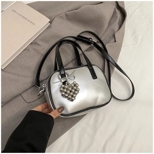 Détail du sac à main argenté avec breloque cœur et poignée en cuir noir élégante