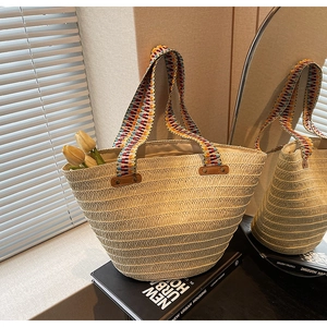 Detail of woven straw tote bag featuring colorful geometric handles and rivet accents