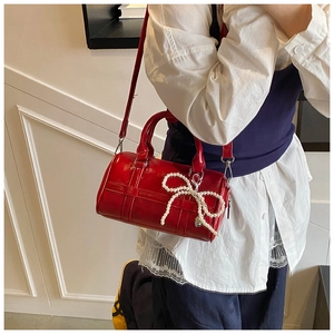 Detail of red glossy pillow bag with pearl bow pendant and silver hardware strap