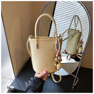 Detail van beige emmertas in getextureerd leer met een parelhanger en schouderband