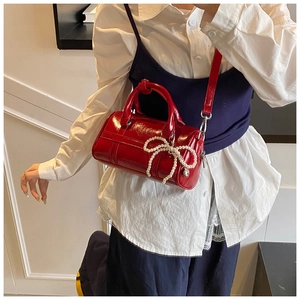 Detail of red patent leather Boston bag featuring a pearl bow and glossy finish